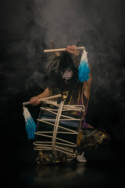 Portrait of an artist on stage. Japanese taiko drummer with drum and drumsticks in outstretched hands on a black background. - Fotografie, Obrázek