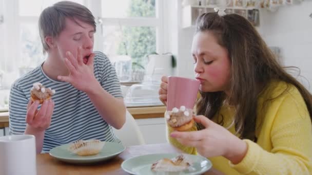 Young Downs Syndrome couple sitting around table with hot drink and cakes at home talking - shot in slow motion - Materiał filmowy, wideo