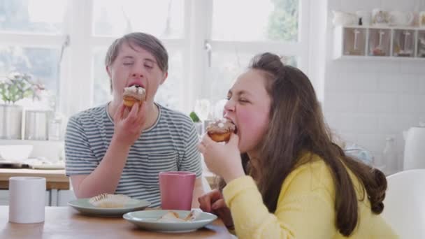 Young Downs Syndrome couple sitting around table with hot drink and cakes at home talking - shot in slow motion - Filmati, video