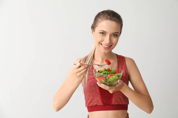 Sportowa kobieta jedząca zdrową sałatkę warzywną na jasnym tle. Koncepcja diety - Zdjęcie, obraz