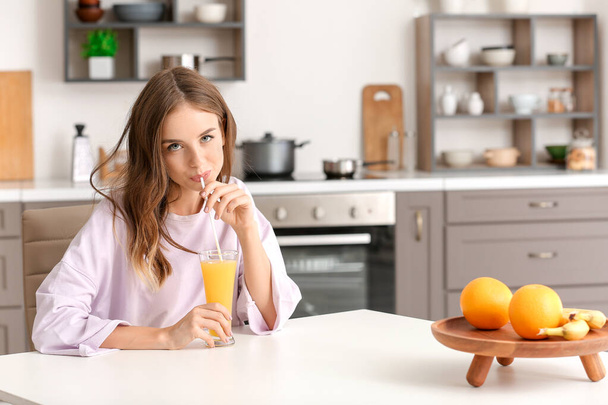Beautiful young woman drinking orange juice in kitchen - Photo, image