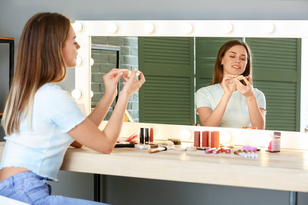Belle jeune femme appliquant le maquillage devant le miroir
 - Photo, image