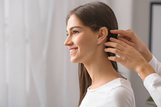 Женщина кладет слуховой аппарат в ухо молодой девушки дома
 - Фото, изображение