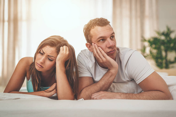 Upset and angry young couple is feeling stressed after quarrel with each other, with an expression of anger and displeased on their faces, lying down on bed. - Photo, Image