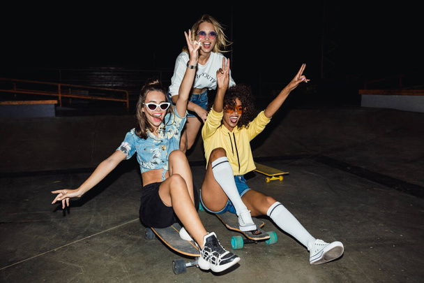 Image of three multinational girls smiling and riding on skatebo - 写真・画像