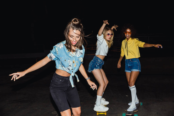 Image of fashion multinational girls smiling and riding skateboa - Foto, imagen