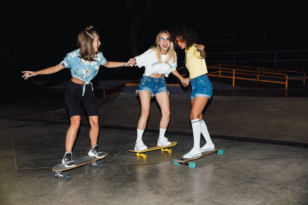 Image of happy multinational girls smiling and riding skateboard - Photo, Image