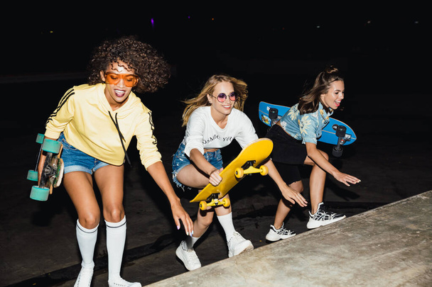 Image of alluring multinational girls smiling and riding skatebo - Фото, зображення