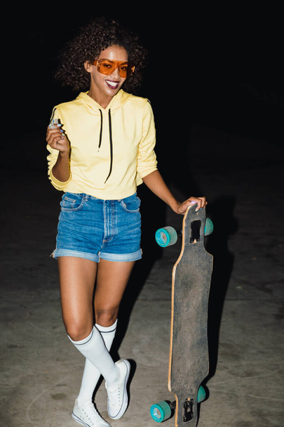 Image of hipster african american girl holding skateboard at nig - Foto, afbeelding