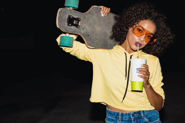 Image of american girl drinking soda and holding skateboard at n - 写真・画像