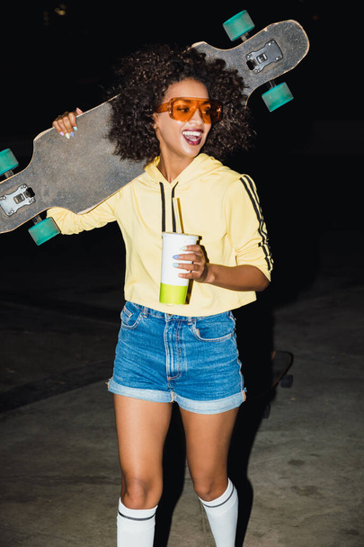 Woman at night walking by street with skateboard. - 写真・画像