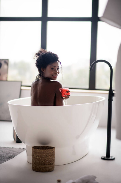 Woman smiling broadly while having bath and holding loofah - Foto, Bild
