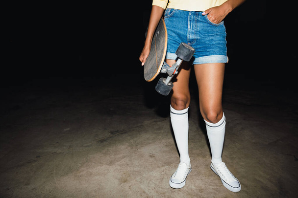 Cropped image of trendy girl in streetwear holding skateboard at - Foto, Imagen