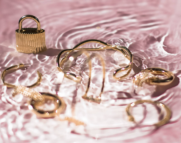 Bracciali dorati, orecchini, anelli, gioielli su fondo acqua rosa
 - Foto, immagini