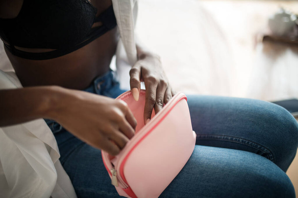 Close up of woman wearing jeans holding pink cosmetics bag - Fotó, kép