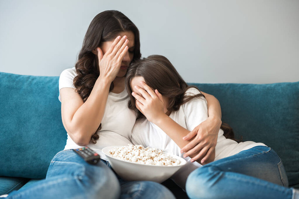 beautiful young mother with her teenager daughter watching movie with violence scene mother and child close their eyes with hands - Фото, изображение