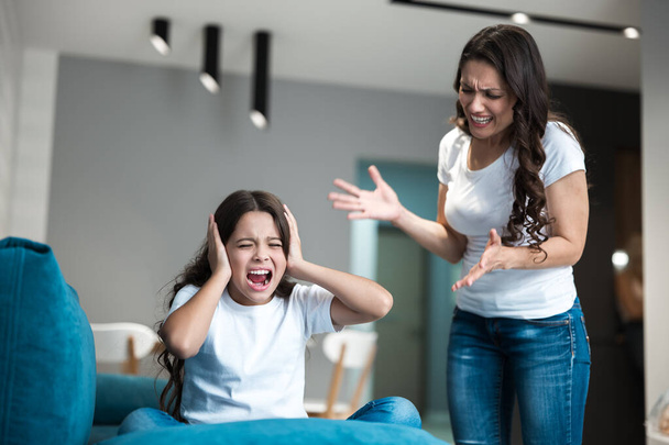 young beautiful woman having an argument with her teen daughter shouting loud in the living room - Photo, image