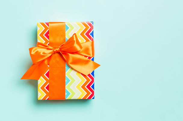 csomagolva karácsony vagy más ünnep kézzel készített ajándék papíron narancssárga szalaggal kék alapon. Jelen doboz, díszítés ajándék színes asztalon, felülnézet másolási hellyel - Fotó, kép