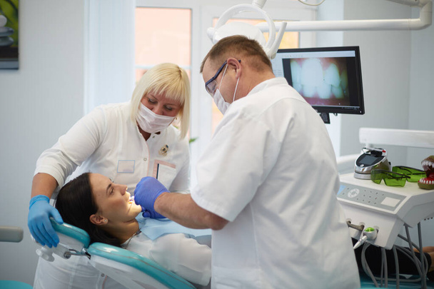 Doktor dişçi genç ve güzel bir kızın dişlerini tedavi ediyor. Dişçinin resepsiyonundaki kız. Doktor dişçi dişleri tedavi eder. - Fotoğraf, Görsel