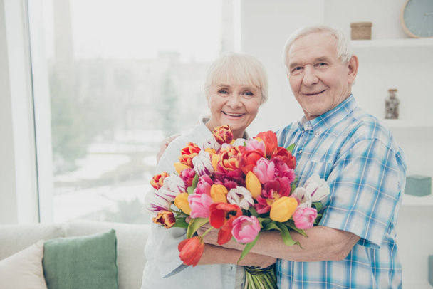 Closeup photo of two adorable aged people cute pair anniversary holiday surprise big red tulips bunch flat indoors - Valokuva, kuva