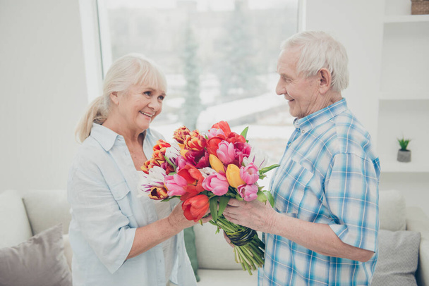 Profile photo of two adorable aged people cute pair anniversary holiday surprise big red tulips bunch bright flat indoors - Fotografie, Obrázek