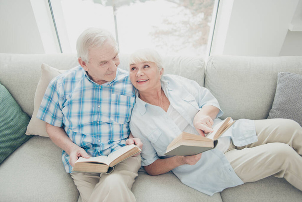 Above high angle view of her she his he two nice attractive cheerful cheery spouses sitting on divan reading new interesting funny book in light white interior living-room indoors - Foto, afbeelding