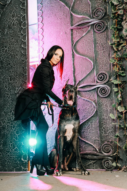 Belle jeune femme posant avec son chien Great Dane dans le studio près de grandes portes noires fond
 - Photo, image