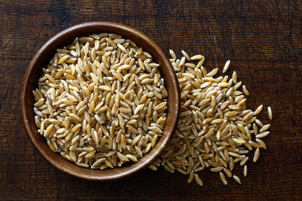 Kamut wheat kernels in dark wooden bowl isolated on dark brown w - Zdjęcie, obraz