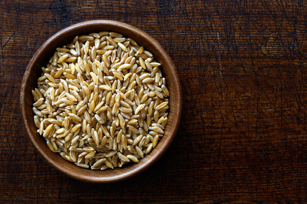 Kamut wheat kernels in dark wooden bowl isolated on dark brown w - Zdjęcie, obraz