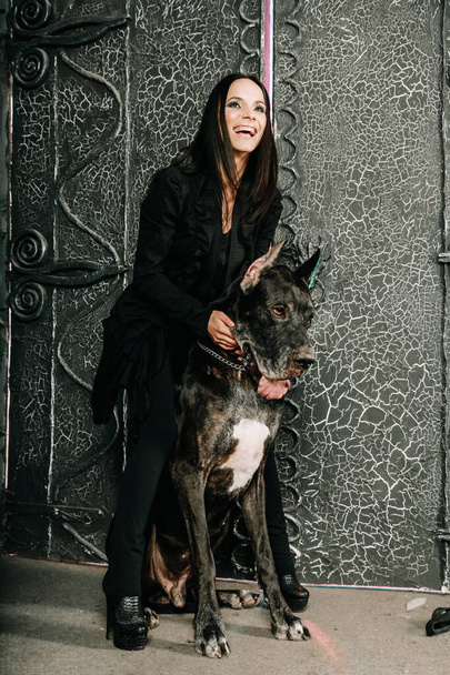 Hermosa joven posando con su gran perro danés en el estudio cerca de grandes puertas negras fondo
 - Foto, Imagen