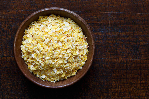 Dry flaked corn in brown wooden bowl isolated on dark wood from  - Foto, Imagem