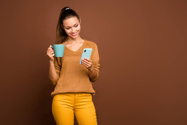 Photo of beautiful attractive cute nice charming fascinating girlfriend chatting via phone holding cup of tea with hand reading feednews isolated over brown pastel color background - 写真・画像