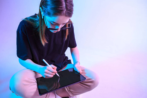 Modern Girl with laptop, tablet computer. Free creativity. A young blogger makes a Home office. Colored Neon light and background. - 写真・画像