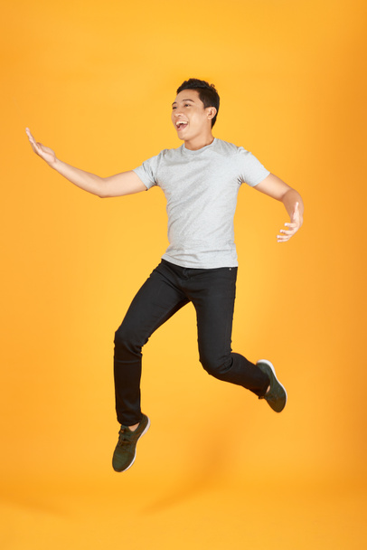 Full length portrait of an excited young man in white t-shirt jumping while celebrating success isolated over orange background - Zdjęcie, obraz