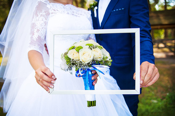 στα χέρια των νεόνυμφων πλαίσιο με ένα γαμήλιο μπουκέτο - Φωτογραφία, εικόνα