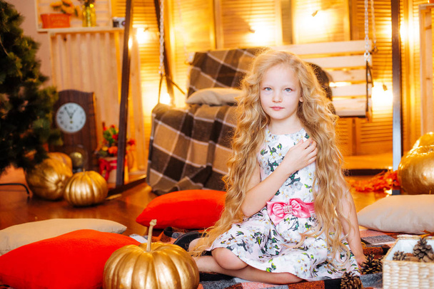 Cute girl of school age with blond long hair in an autumn studio with yellow leaves, plaids, pumpkins and apples - Foto, Bild