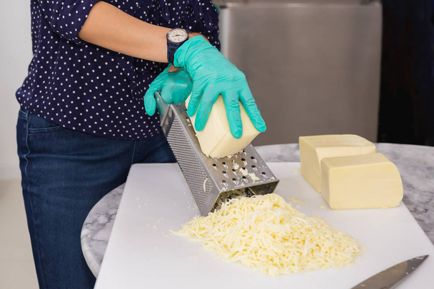 Жінка з зеленими рукавичками терти сир на кухонному столі
. - Фото, зображення
