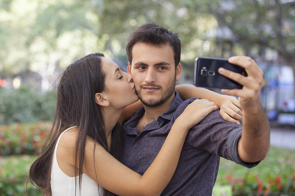 Happy young couple kissing and posing in park nature, taking selfie by mobile phone  - Photo, Image