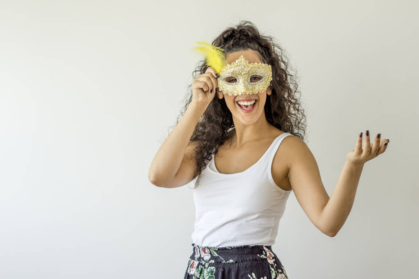 Νεαρή γυναίκα χαμογελά κρατώντας μάσκα καρναβαλιού σε λευκό φόντο - Φωτογραφία, εικόνα