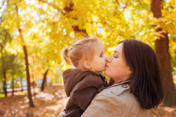 Familie in het herfstpark tussen gele bladeren. Jonge moeder met een dochtertje spelen met bladeren in het herfstpark. Herfst stemming - Foto, afbeelding