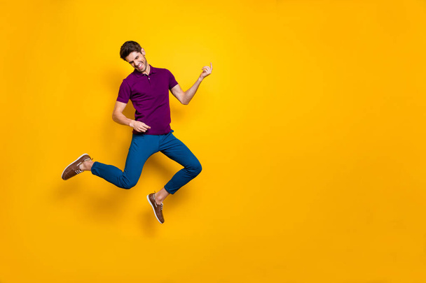 Photo of cheerful crazy ecstatic overjoyed man pretending to be playing imaginary guitar wearing blue pants trousers shoes isolated over yellow vivid color background - Foto, afbeelding