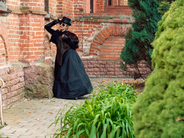 niña en un vestido negro sobre un fondo de una pared de ladrillo en otoño
 - Foto, imagen