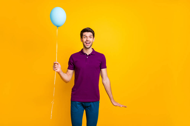 Photo of cheerful positive casual handsome man holding air ball of helium with hands wearing pants trousers blue isolated over vivid color background - Foto, afbeelding
