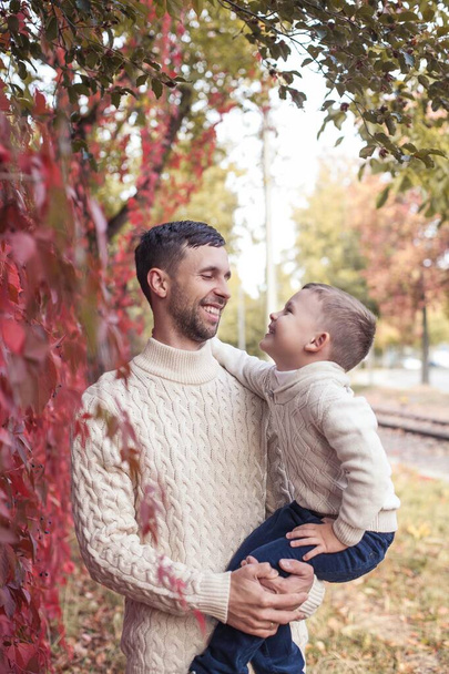 お父さんと mvlenky の息子は、秋の公園を散歩します。明るく、暖かい秋。赤の葉。居心地の良い。お父さんと息子のニット セーターでの肖像画. - 写真・画像
