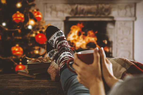 Legs in winter christmas socks on wooden top board with fireplace background in cozy home interior. - Φωτογραφία, εικόνα