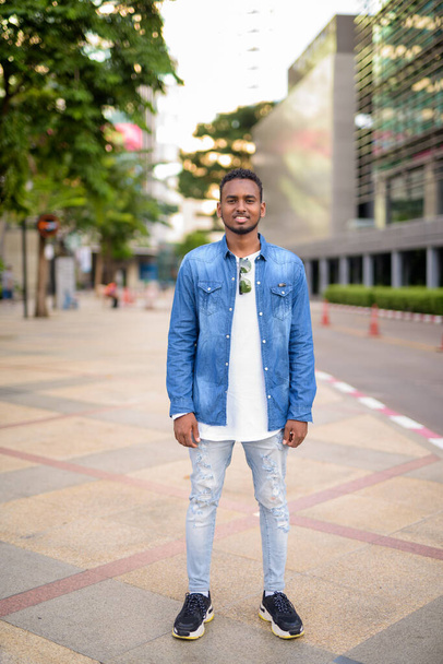Full body shot of happy young African bearded man smiling in the city streets - Φωτογραφία, εικόνα