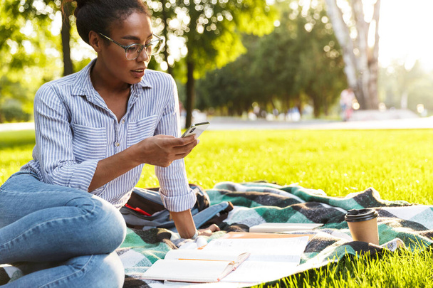 Image of african american woman holding smartphone and studying  - Foto, afbeelding