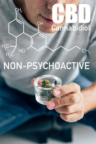 cropped view of man in t-shirt looking at medical cannabis in glass container with non-psychoactive cbd illustration - Фото, зображення