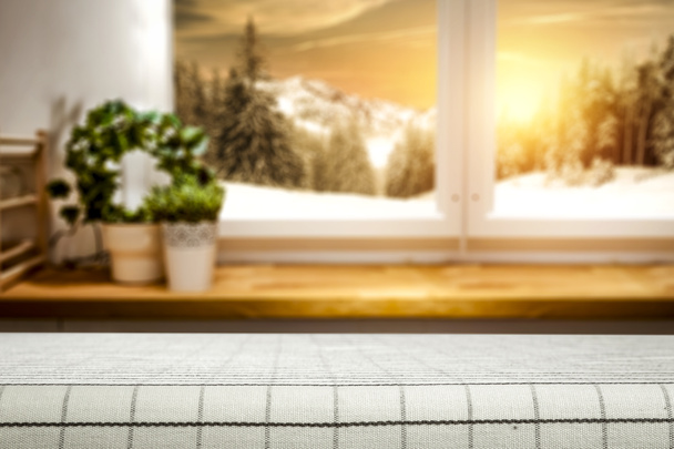 Blurred nevado invierno sol paisaje fuera de la ventana cocina con mesa superior para productos y decoraciones
. - Foto, Imagen