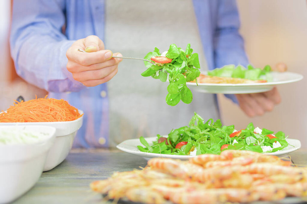 Mann in blauem Hemd, dessen Hände und Bauch man sieht, wie er Gemüse mit einer Gabel serviert, wobei der Hintergrund unscharf ist. - Foto, Bild
